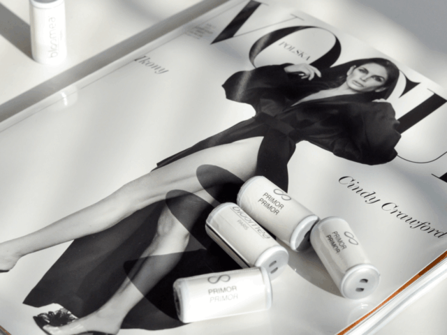 Magazyn Vogue Polska z czarno-białą okładką przedstawiającą elegancko ubraną kobietę w stylowym płaszczu. Na okładce umieszczono produkty marki Bloomea Paris, w tym opakowanie "Embout Primor" oraz kilka mniejszych tubek, na tle marmurowego stołu i złotej wstążki. Innowacje kosmetologiczne na BiNatural 2023