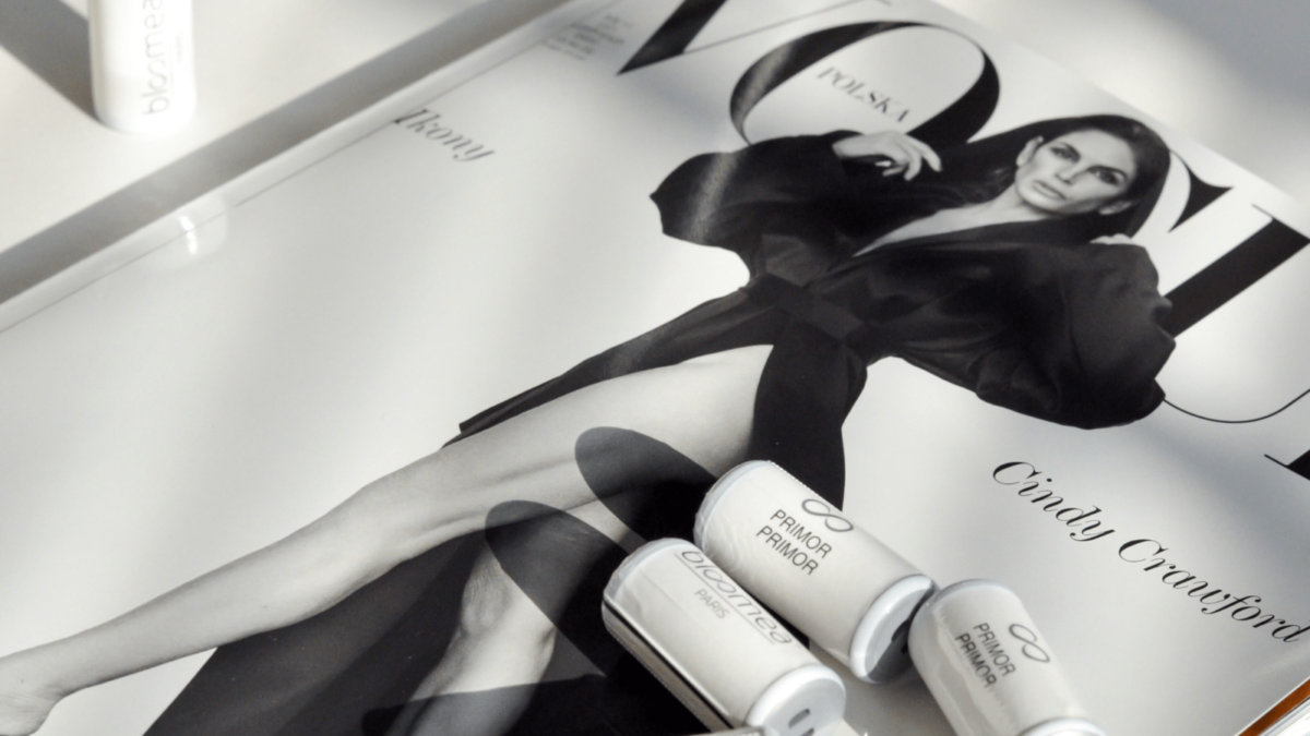 Magazyn Vogue Polska z czarno-białą okładką przedstawiającą elegancko ubraną kobietę w stylowym płaszczu. Na okładce umieszczono produkty marki Bloomea Paris, w tym opakowanie "Embout Primor" oraz kilka mniejszych tubek, na tle marmurowego stołu i złotej wstążki. Innowacje kosmetologiczne na BiNatural 2023