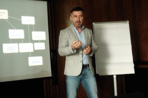 Mężczyzna prowadzi prezentację przy slajdzie z organizacją struktury firmy – tekst alternatywny.