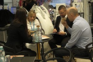 Grupa osób w formalnych strojach przy stoliku, w tle urządzenia beauty